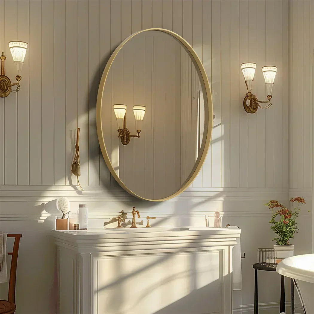 Oval vanity mirror with brushed gold frame in elegant bathroom setting.