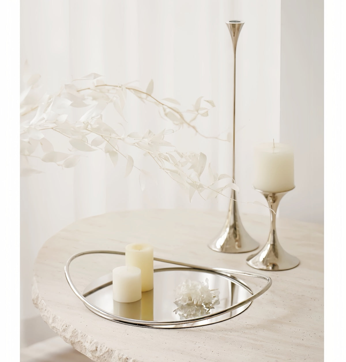 Decorative setting with a mirror tray, candles, and tall candle holders on a light surface.