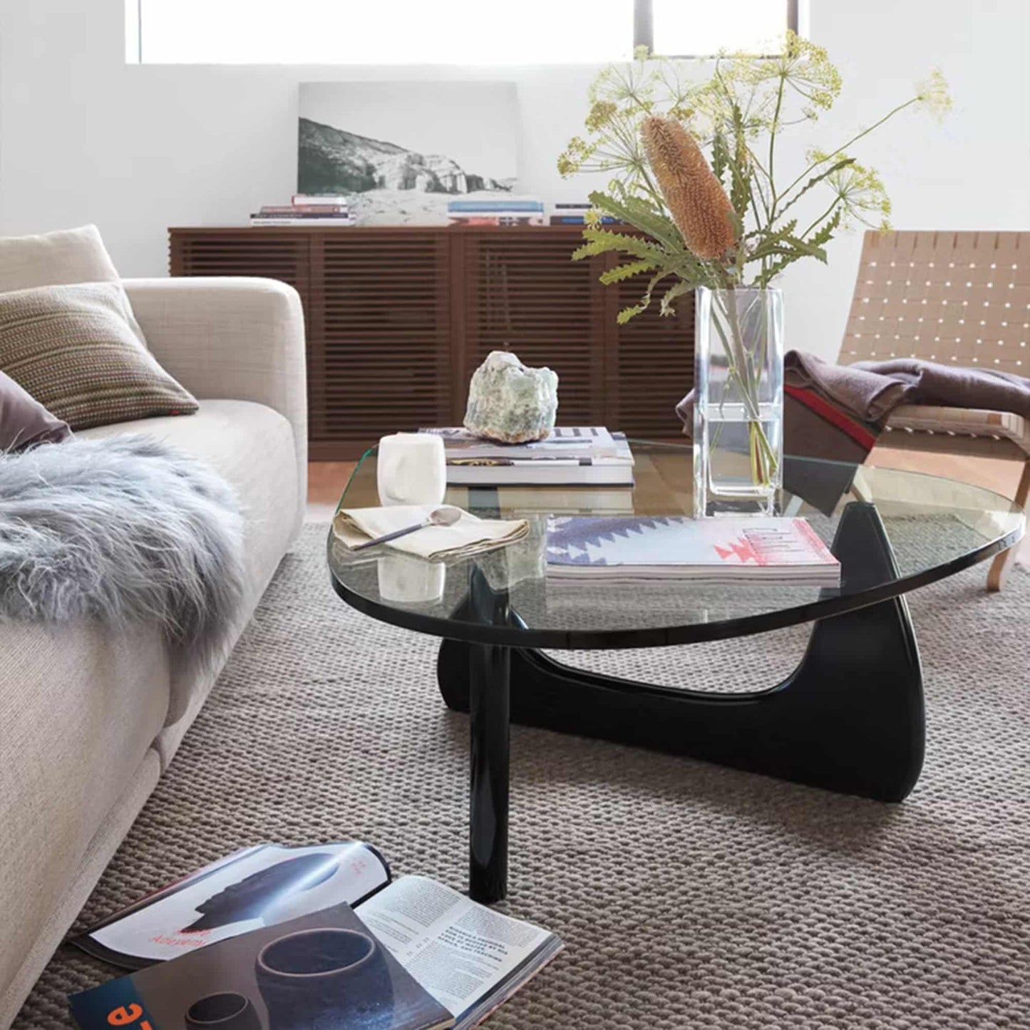 Noguchi Coffee Table with sculptural wooden base and clear glass top in modern living room setting.