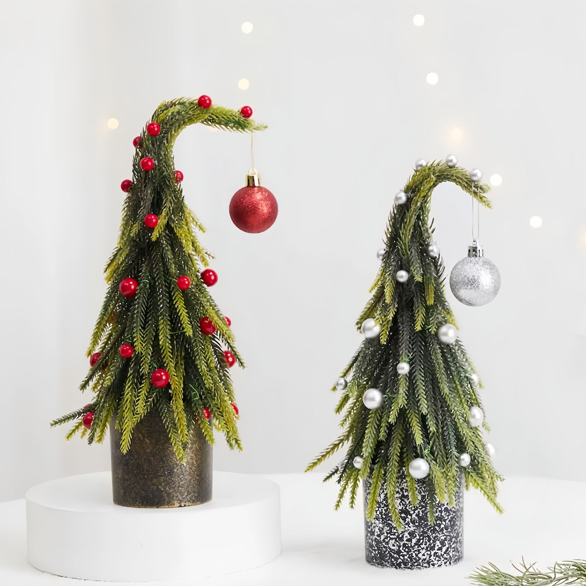 Two decorative Christmas trees made from greenery and ornaments on a white background