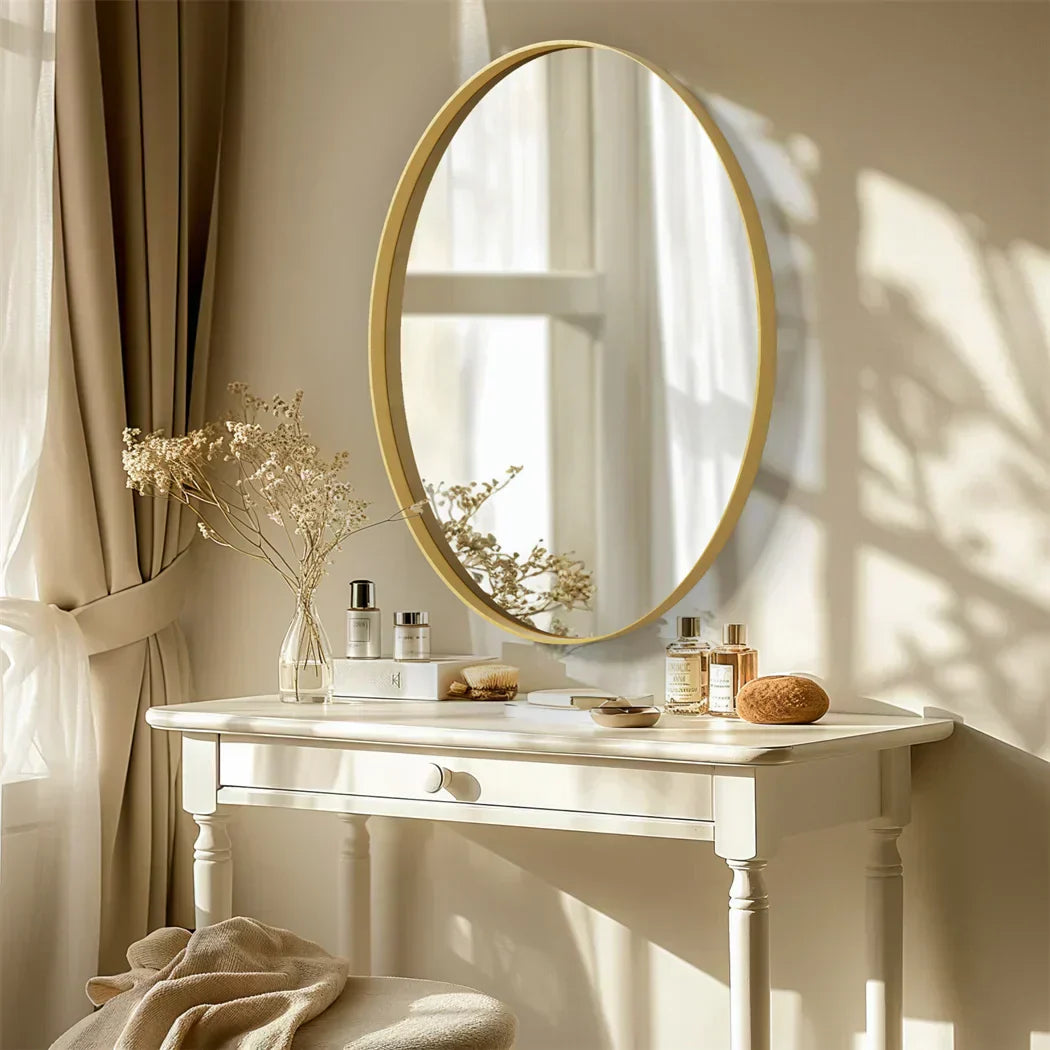 Oval vanity mirror with sleek gold frame, wall-mounted above a white table, reflecting soft ambient light.