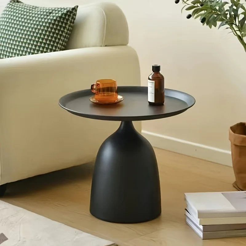 Contemporary round side table with sleek black metal design placed beside a sofa, styled with decor items.