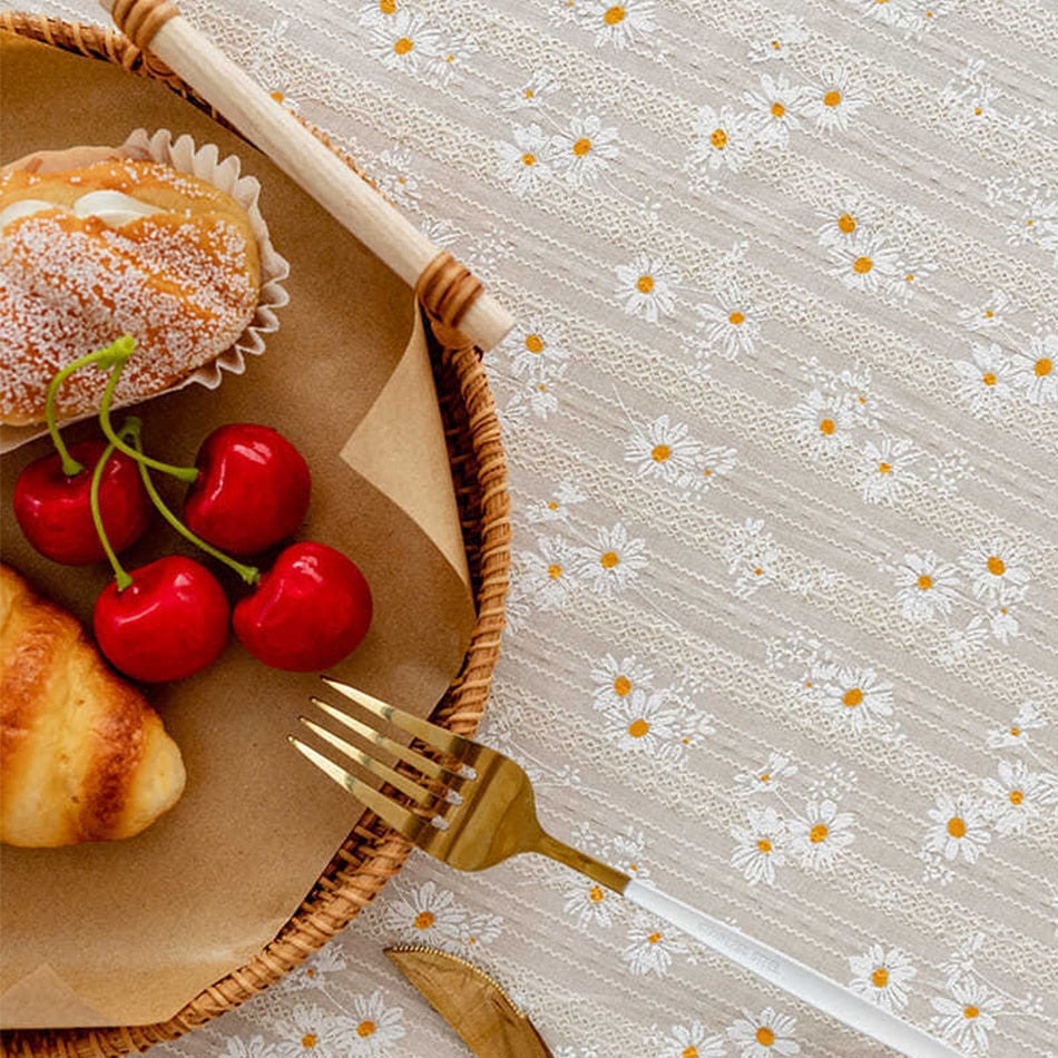 White tablecloth with floral daisy pattern and tassels under a basket with pastries and cherries.