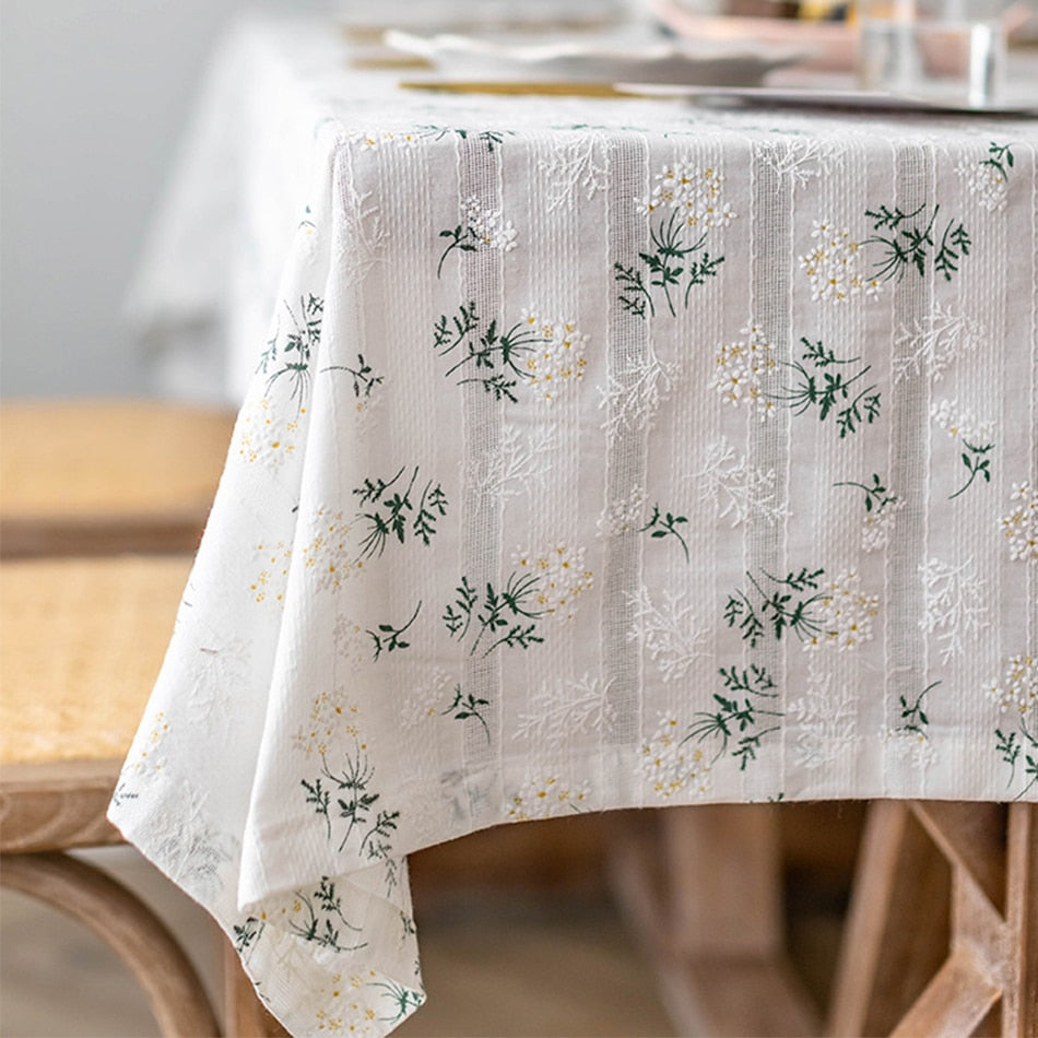 White tablecloth with floral daisy pattern and tassels, elegant cotton decor.