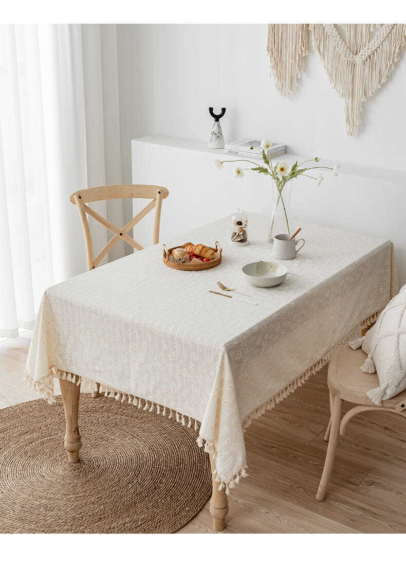 White tablecloth with floral daisy pattern and tassels on a dining table.