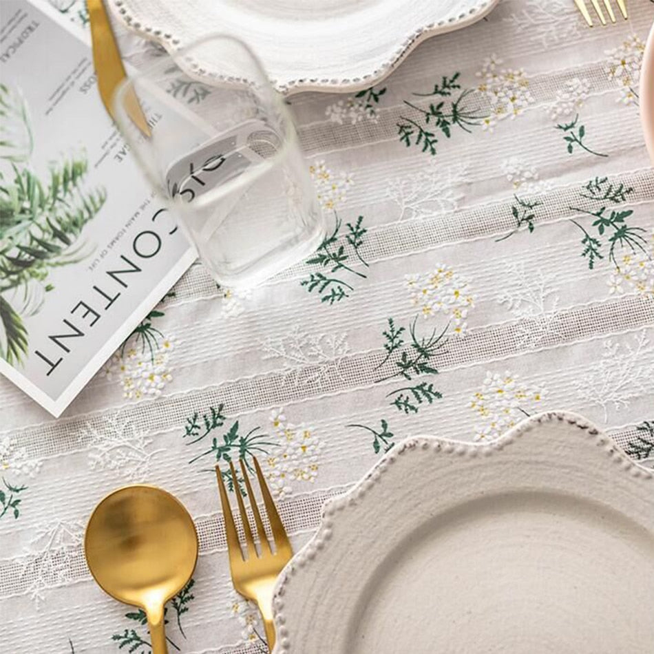 White tablecloth with floral daisy pattern and tassels, elegant cotton decor for tables.