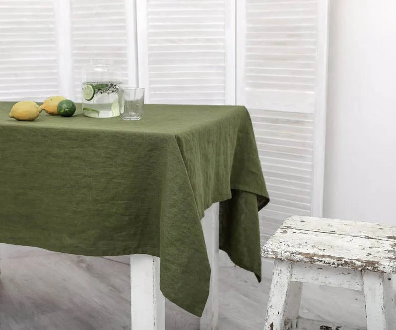 Green rectangle linen tablecloth on dining table with fruits and drink, minimalistic decor.