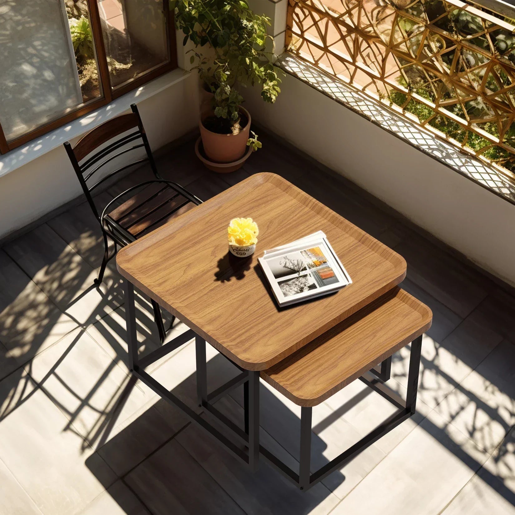 Modern square coffee table set of two in walnut wood and black metal, placed adjacent to a chair on a sunny patio.