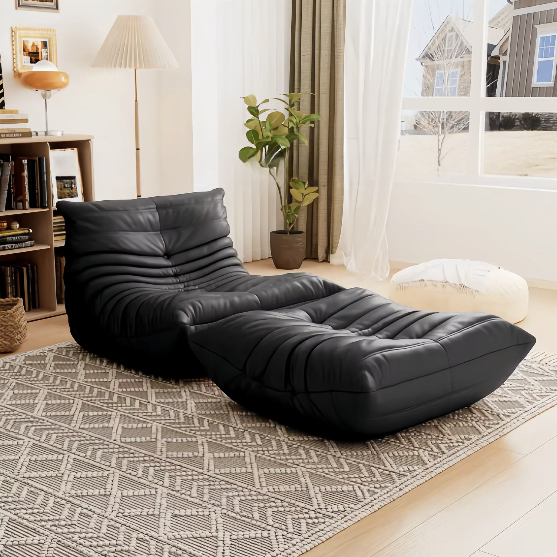 Togo Fireside Chair and Foot Stool set in black suede upholstery, enhancing a modern living room with soft natural lighting.