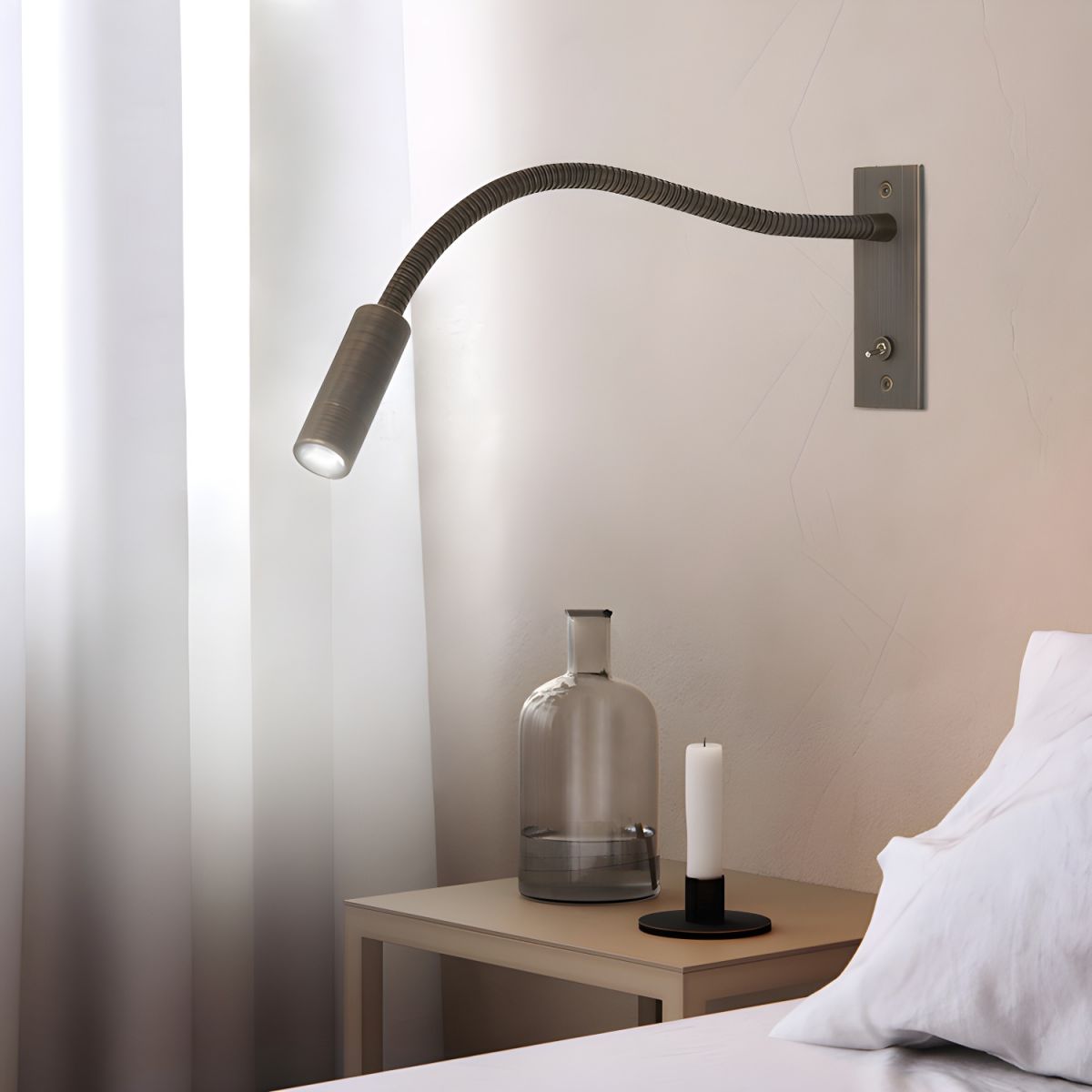 Wall-mounted lamp with flexible arm on a neutral wall near a table with a vase and candle.