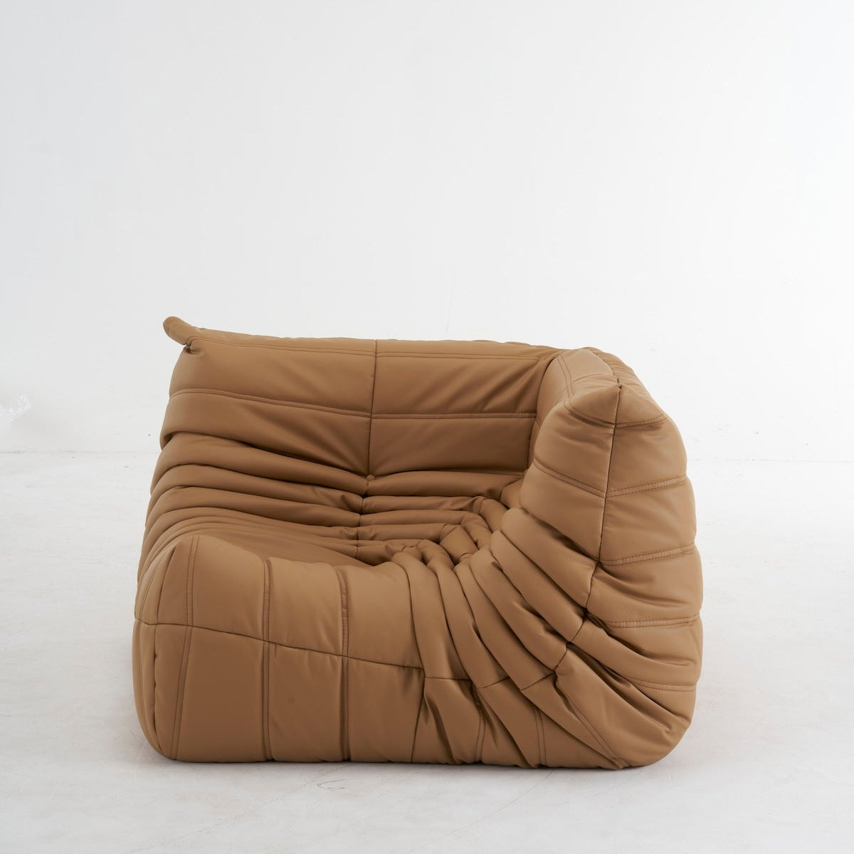 A modern, low-profile lounge chair upholstered in a warm camel brown bouclé fabric, featuring a heavily ruched and pleated design, set against a seamless white studio background.