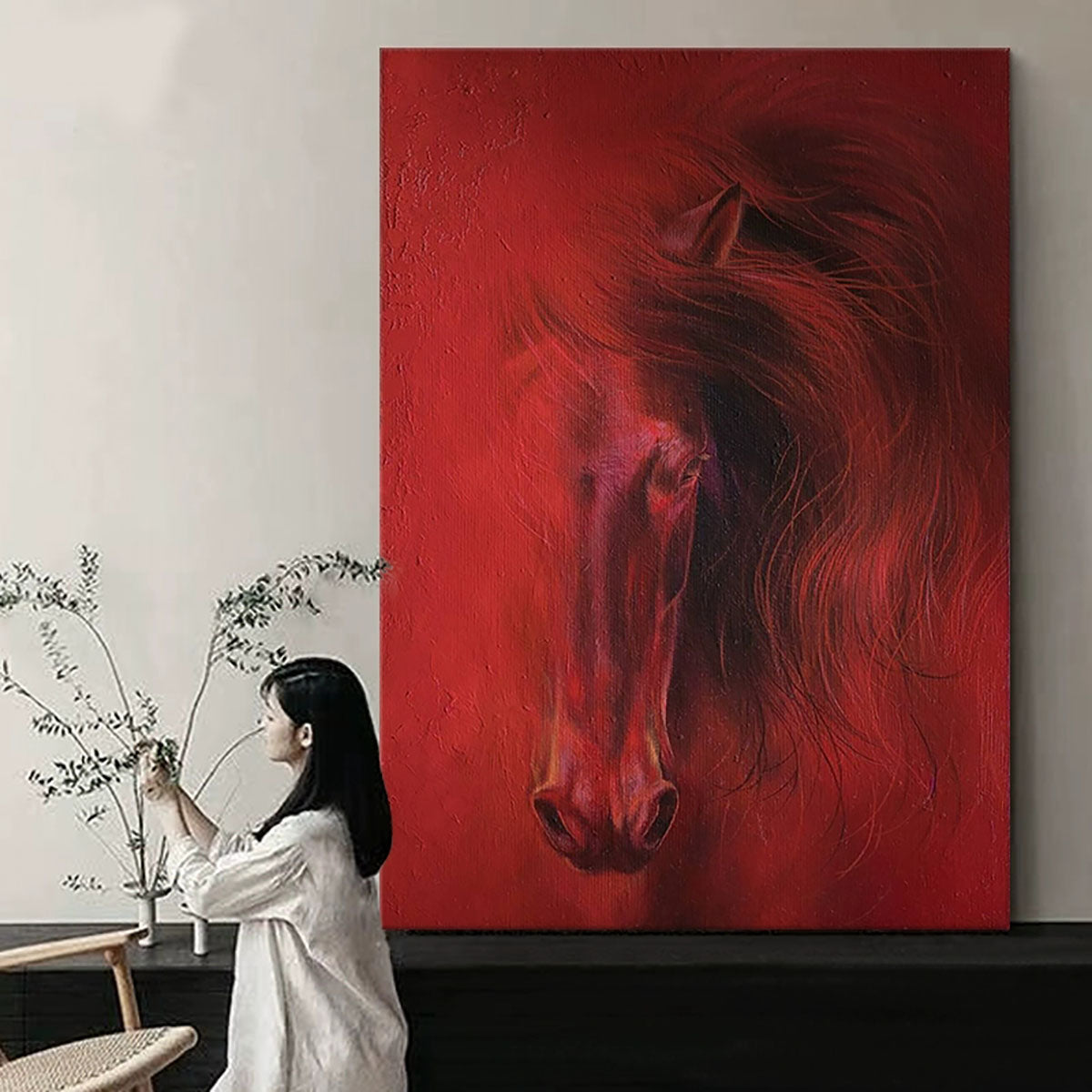 Woman sitting in front of a large red painting of a horse in a room with minimal decor.
